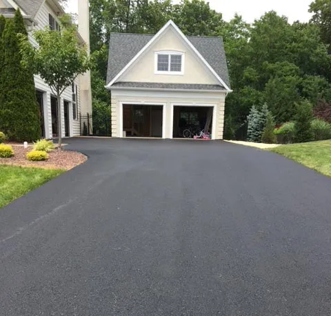 Freshly paved black asphalt driveway leading to a white two-car garage with trees around.